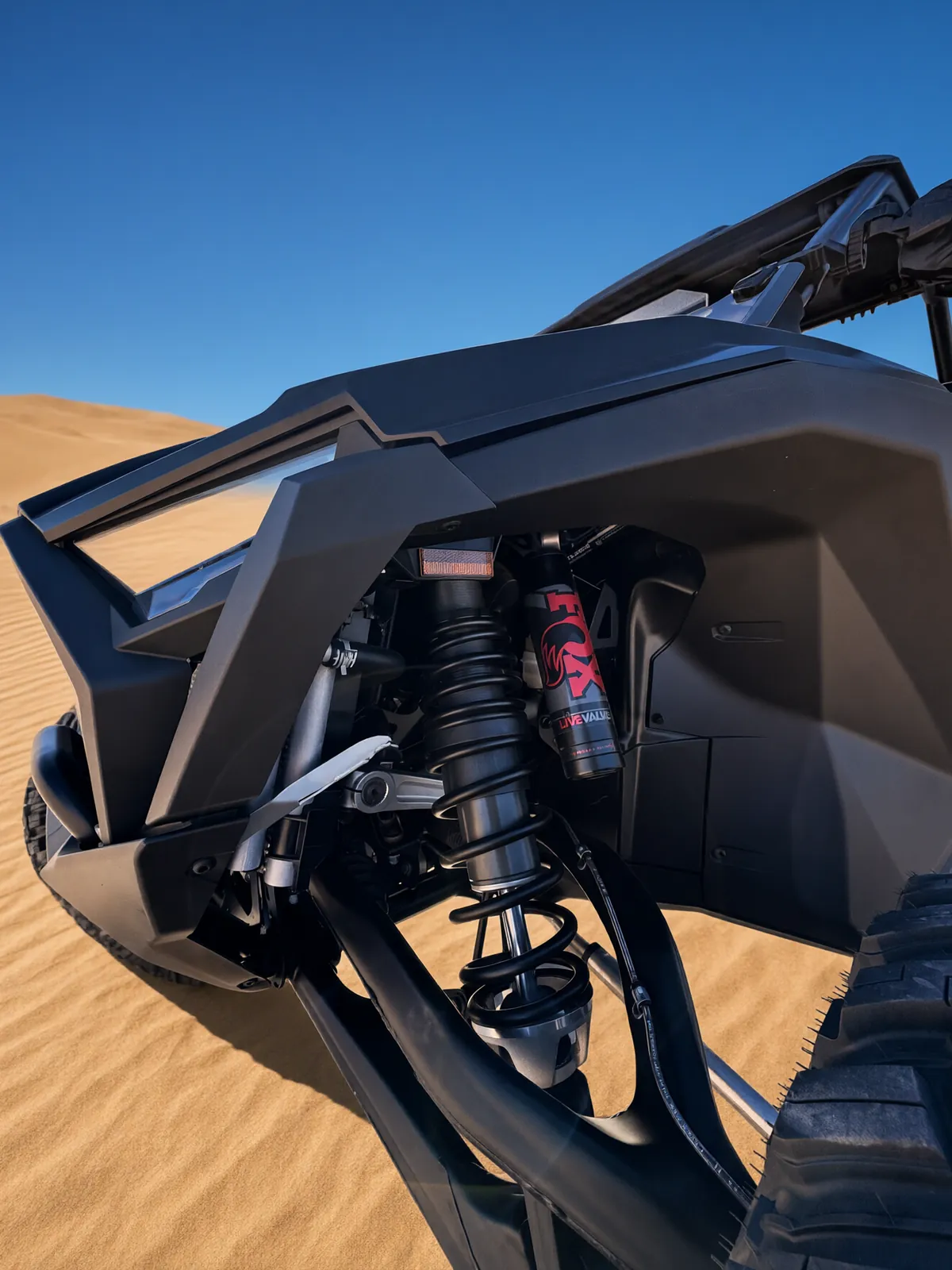 Close-up of the RZR Pro S Ultimate "Ninja" front suspension on the sand dunes: the red FOX LIVE VALVE shock, black coil spring and suspension arms