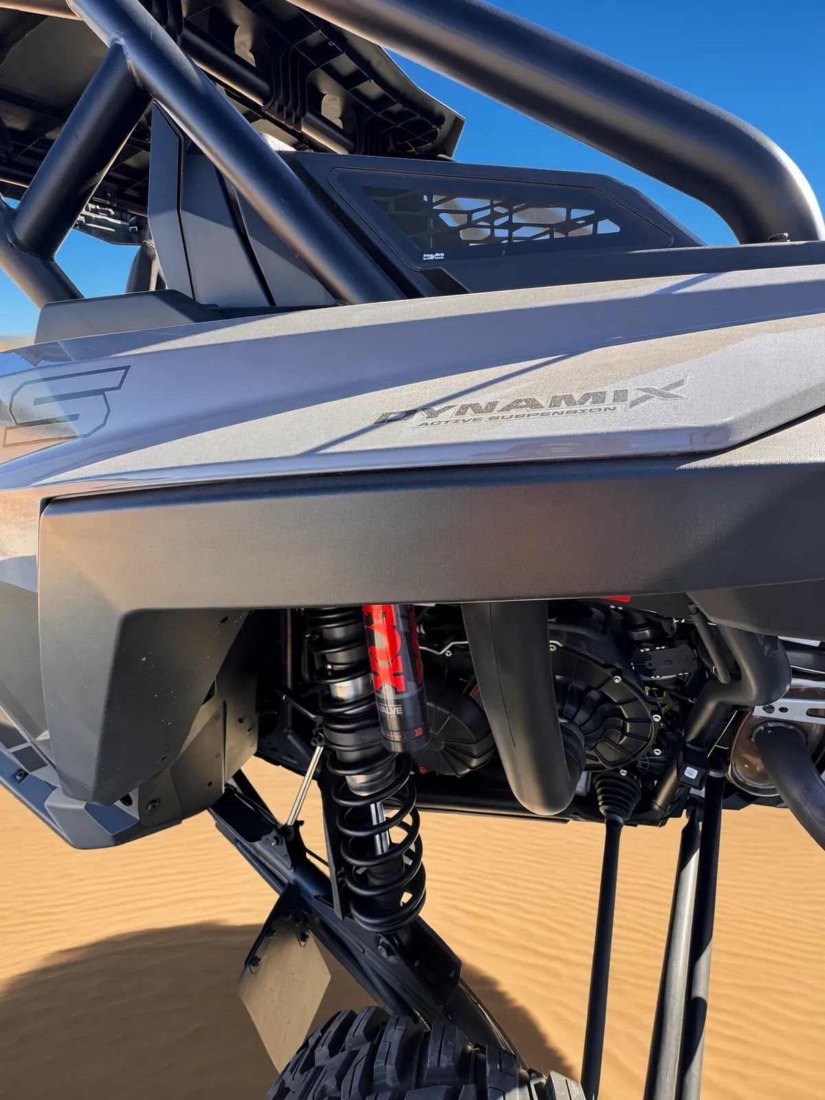 Close-up of the RZR Pro S Ultimate "Ninja" rear suspension on the sand dunes: the red FOX LIVE VALVE X2 shock and coil spring below the DYNAMIX Active Suspension decal