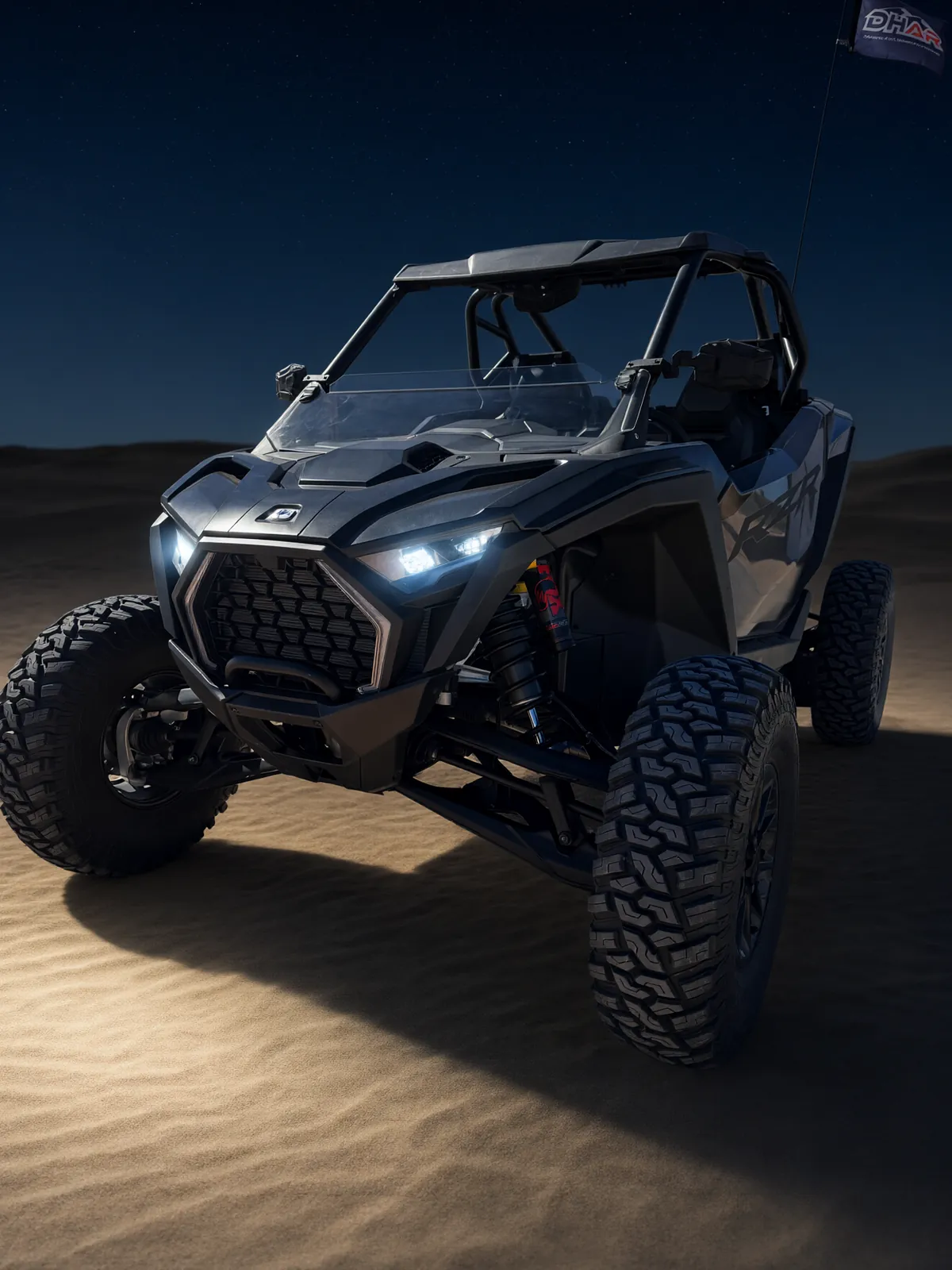 Polaris RZR Pro S Ultimate "Ninja" on sand dunes at night under a starry sky with its headlights and LED fang accent lights around the grille glowing, front view showing its black grille and LED headlights